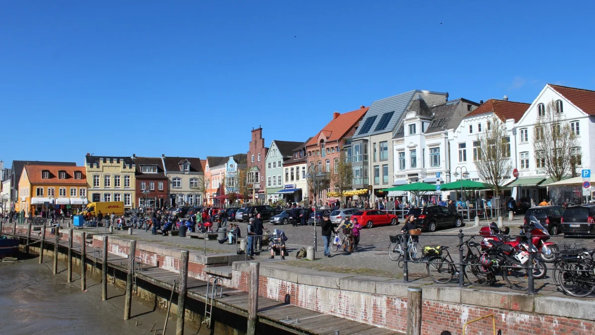 Gezellige haven in Friesland met kleurrijke gevels, terrassen en mensen die wandelen of fietsen op een zonnige dag.