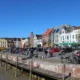 Gezellige haven in Friesland met kleurrijke gevels, terrassen en mensen die wandelen of fietsen op een zonnige dag.