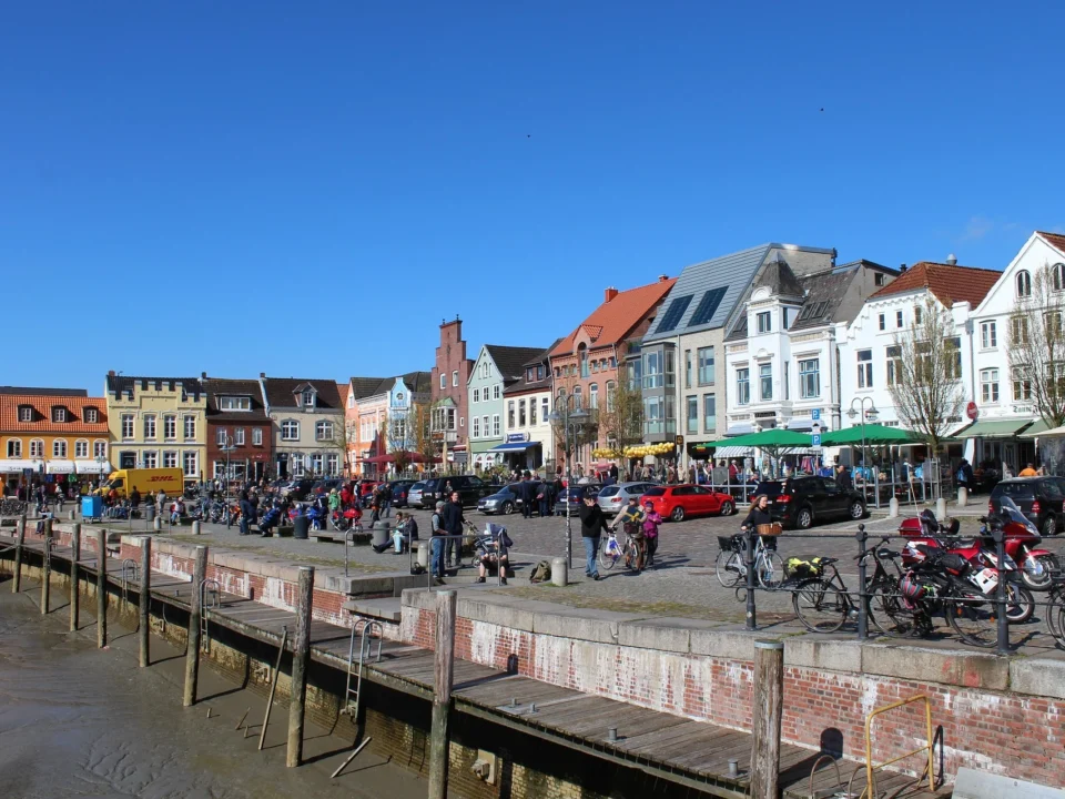 Gezellige haven in Friesland met kleurrijke gevels, terrassen en mensen die wandelen of fietsen op een zonnige dag.